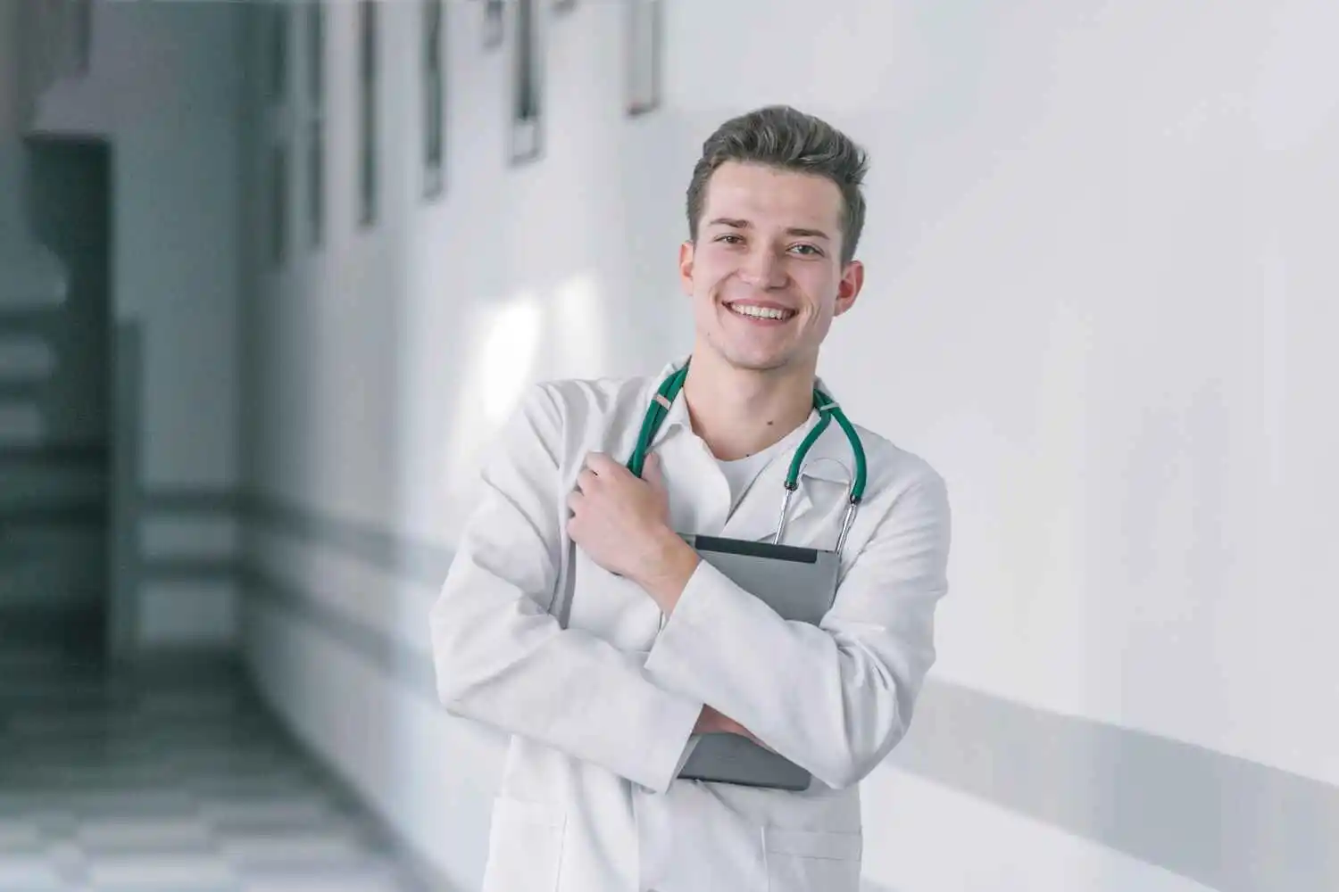 A close-up of a healthcare worker in uniform, with a stethoscope and hospital in the background.